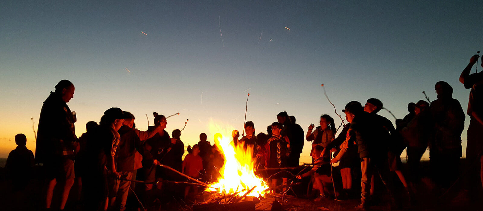Scouts and leaders gathered around a campfire at dusk